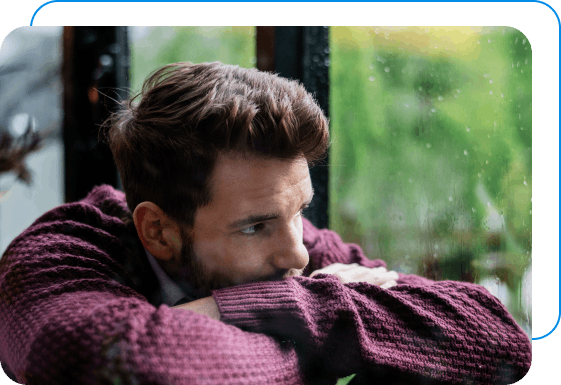 Man with an eating disorder sadly looking out of a window while it’s raining.